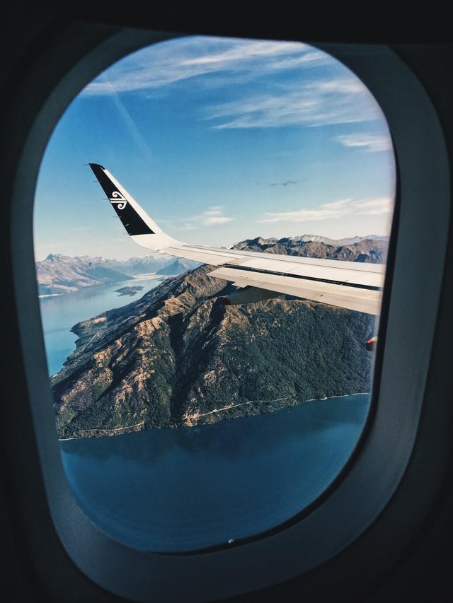 A stunning view outside of a plane window with the airplane wing and mountains and ocean beneath