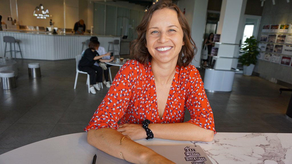 A smiling woman in a coffee shop with a closed computer in front of her getting ready to start her day of remote work