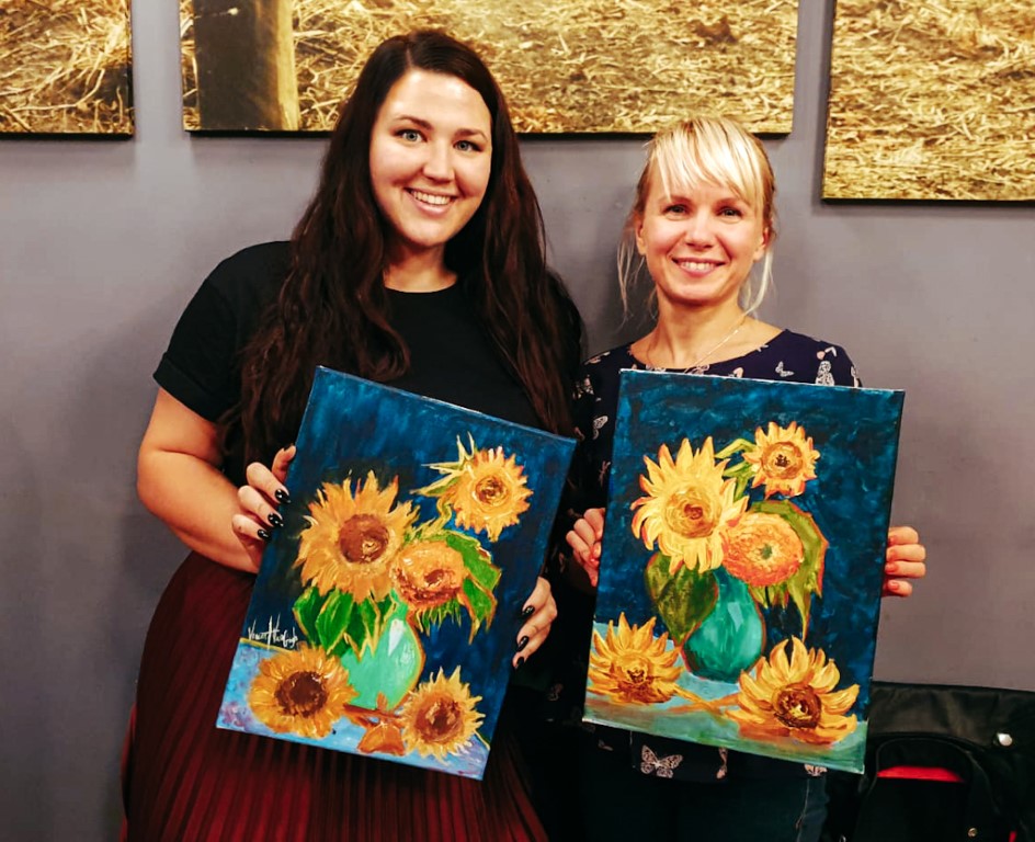 two women holding up their paintings of sunflowers on a fun night out