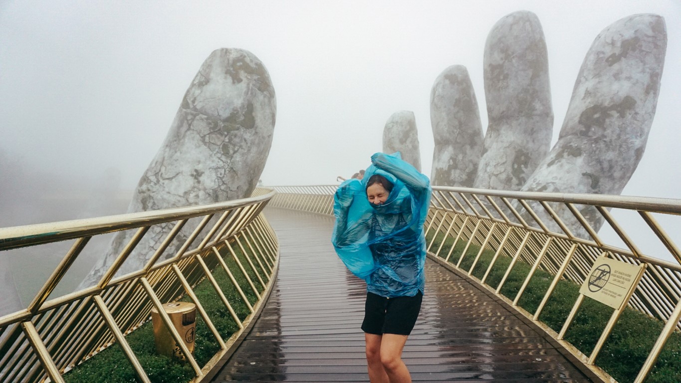 A woman on the golden hands bridge in Da Nang, Vietnam in a storm caught in her poncho