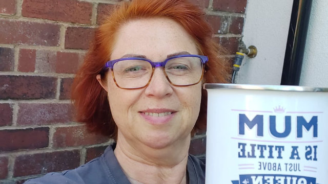 a mom wearing glasses holding a mug taking a selfie outside her house