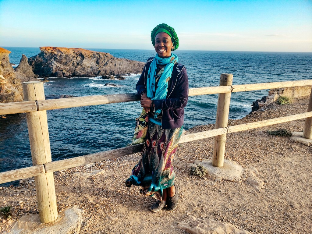 A Black American women enjoying smiling over a railing on the rocky coast of Spain
