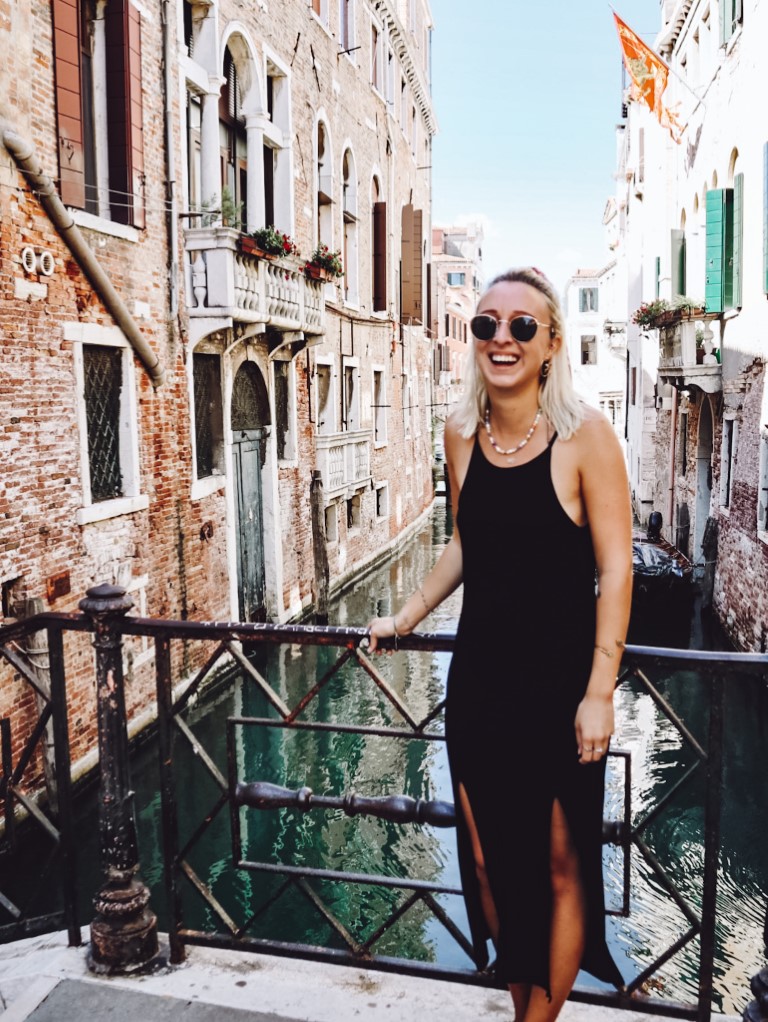 A smiling blond woman in Venice posing on a bridge over the small canals