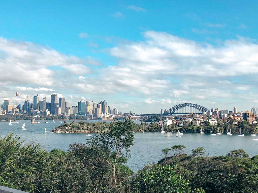 A skyline view of Sydney, Australia on a sunny afternoon with the water, opera house and blue skies