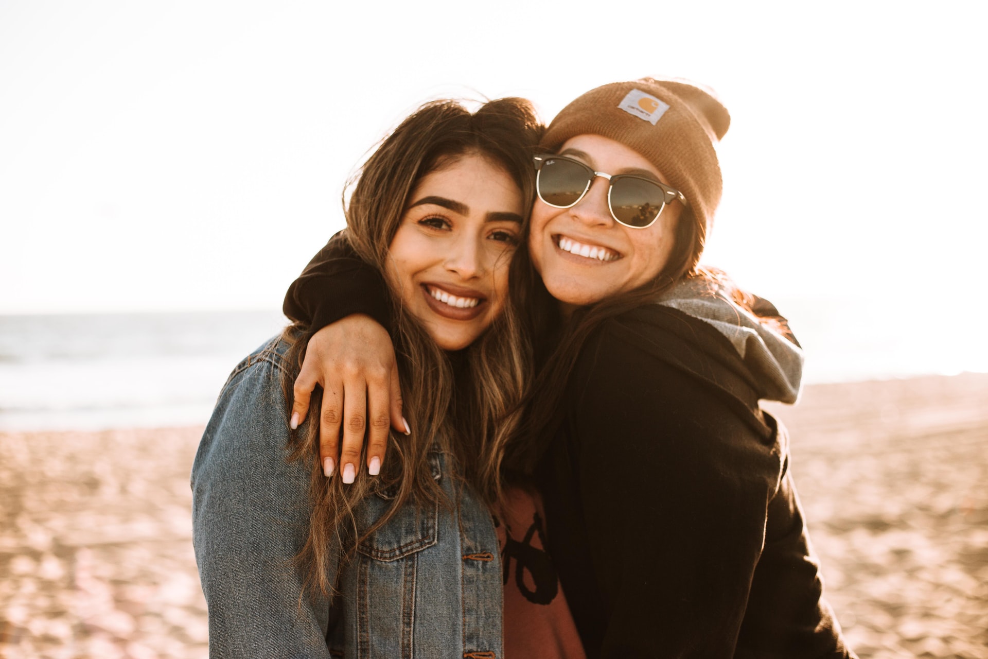 two happy women smiling at the camera hugging each other with the sun setting in the background