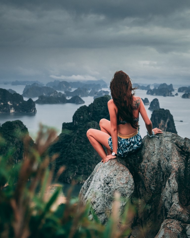 a woman sitting on a rock overlooking a rocky coastline in southeast asia