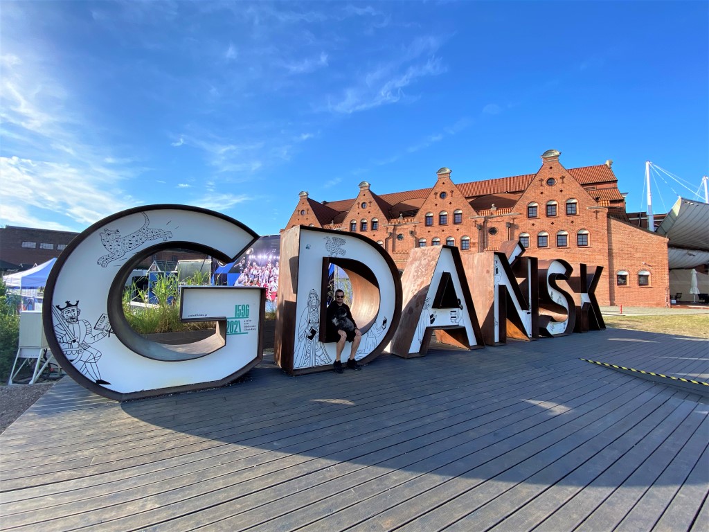 A tourist and in his dog sitting in the big Gdansk sign while visiting the city 