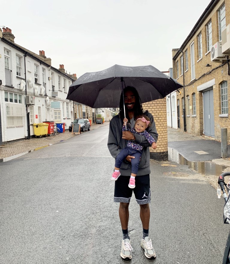 a dad holding his daughter smiling in the rain under an umbrella