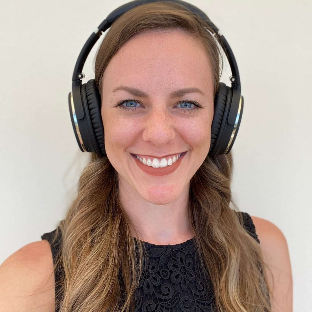 A close up picture of a woman smiling in the camera, wearing big headphones