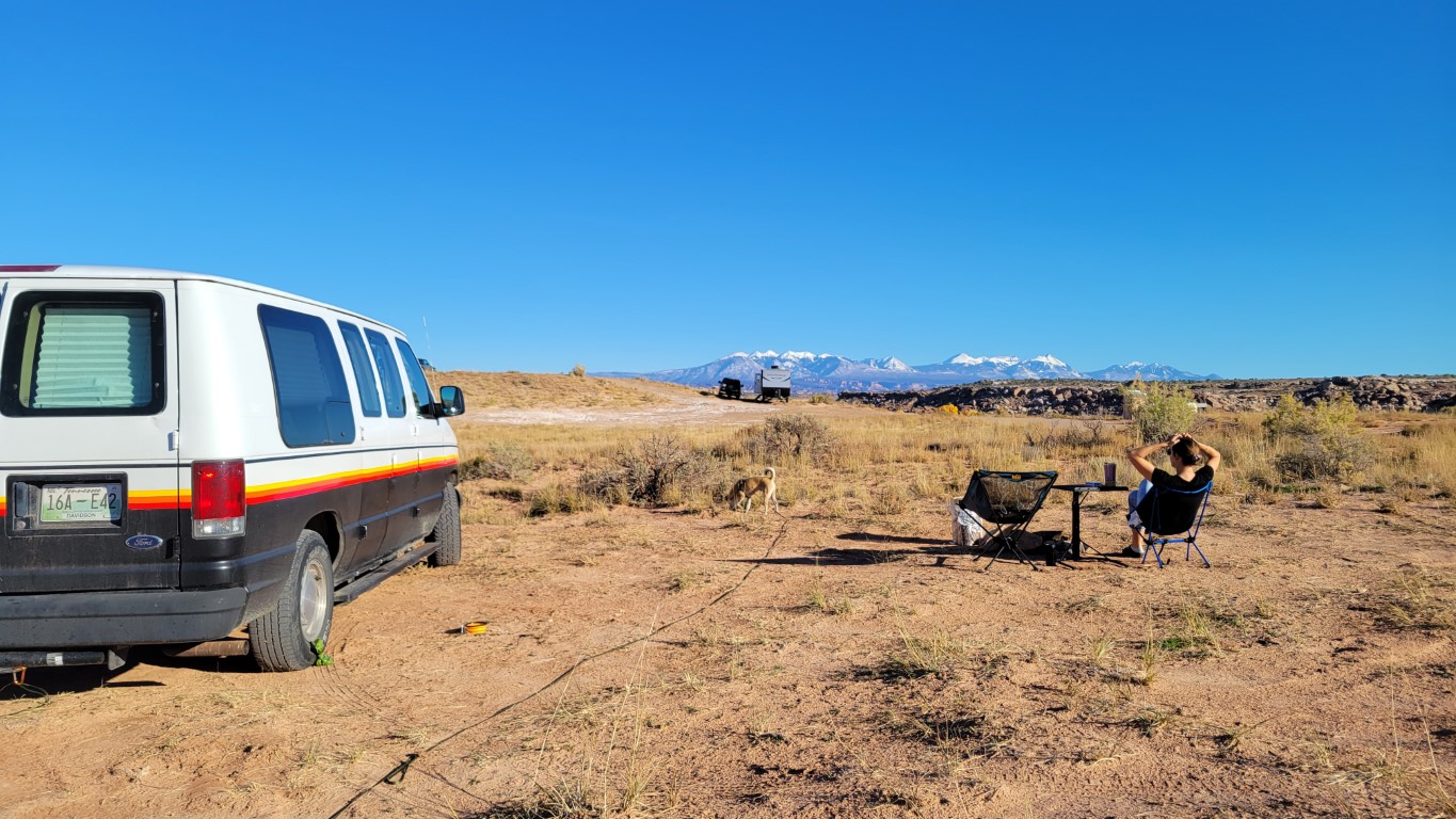 a woman sitting at a campsite with her van parked beside her in Moab, Utah