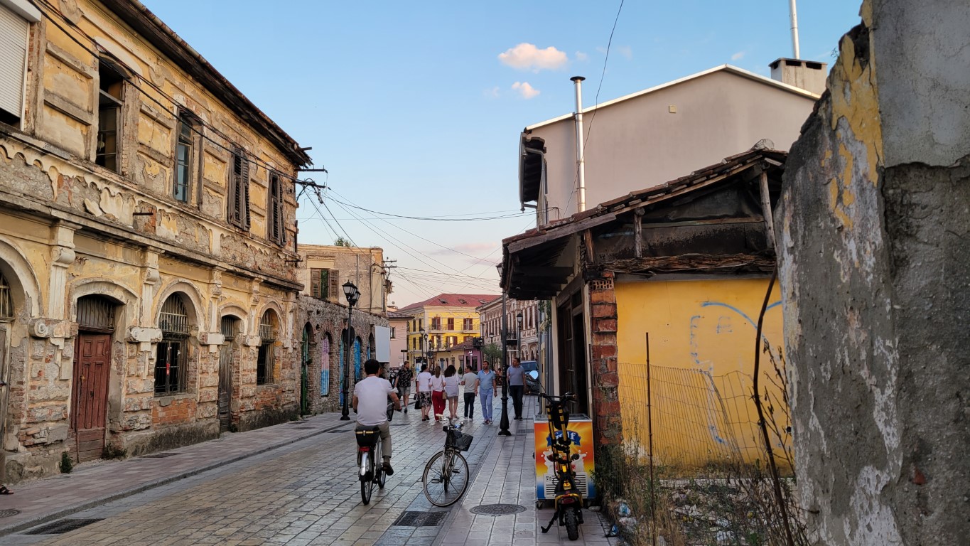 a side street in Shkoder, Albania with people walking and a man on a bicycle