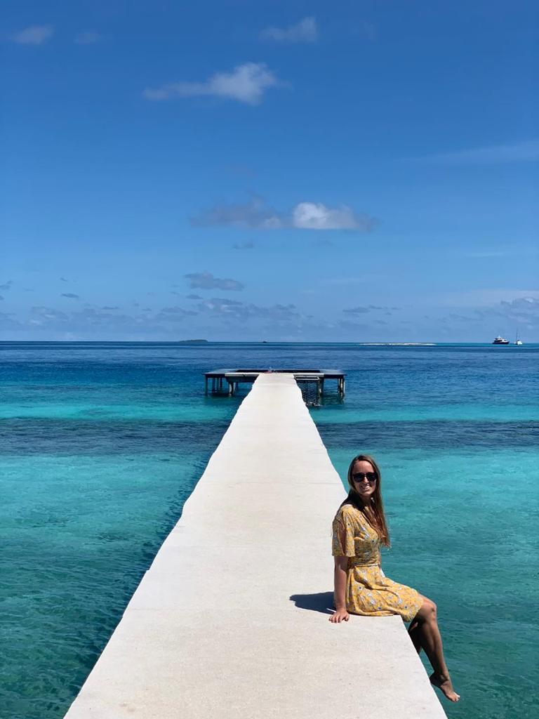 A woman sitting in a yellow dress on a long deck in the Maldives