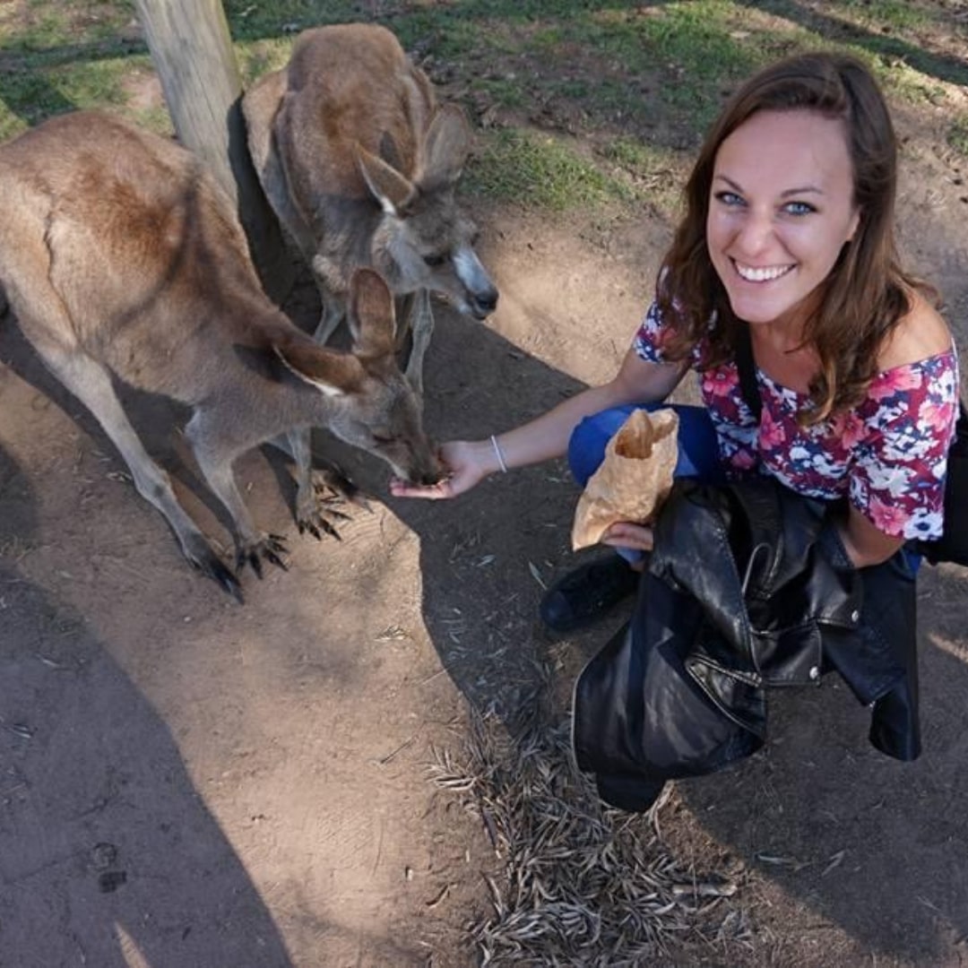 a woman smiling at the camera while feeding two kangaroos
