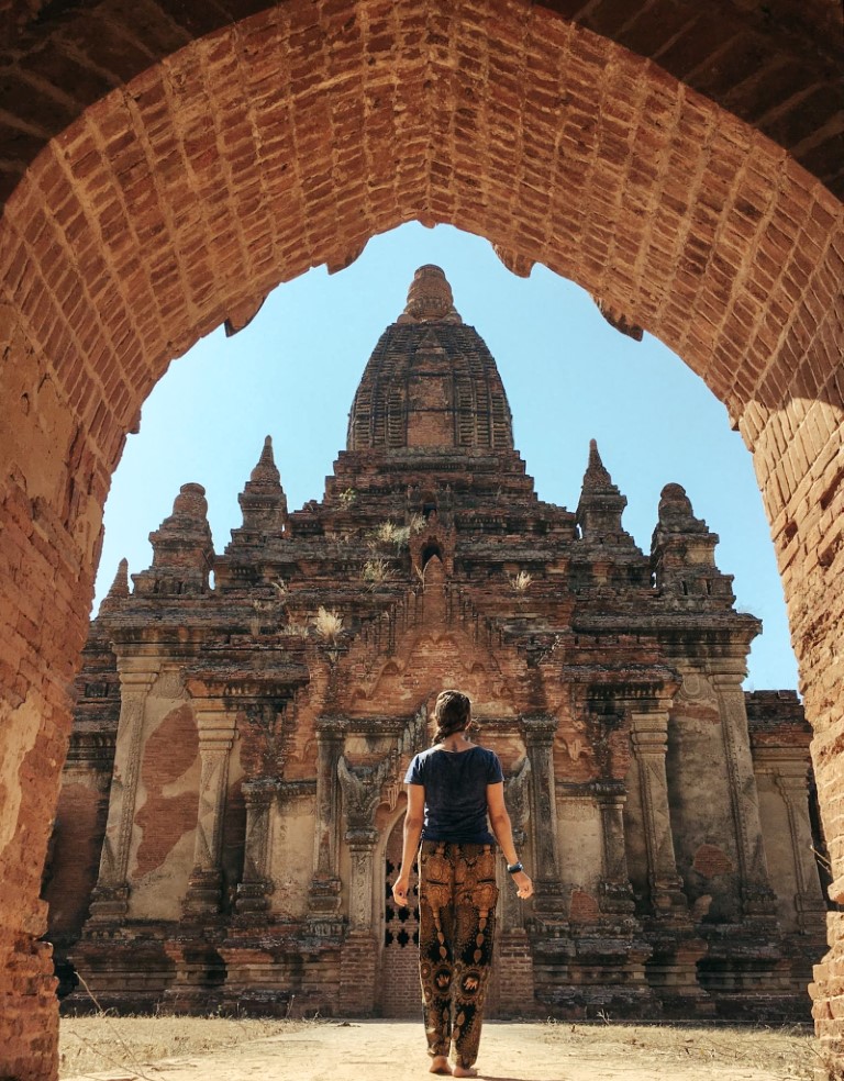 A barefoot woman standing in front of a temple in Myanmar with her back to the camera