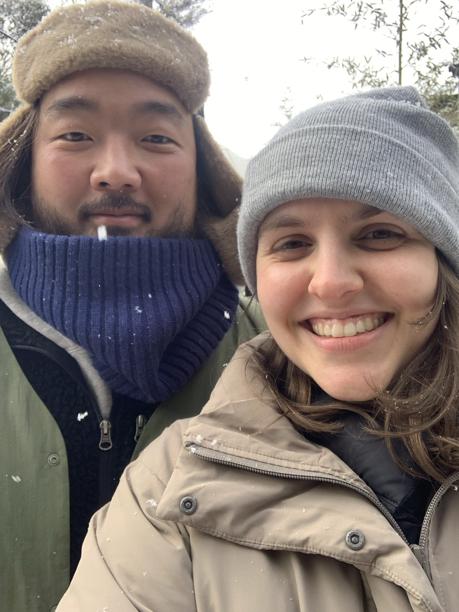 Robyn and her husband in winter hats, smiling, with snow falling.