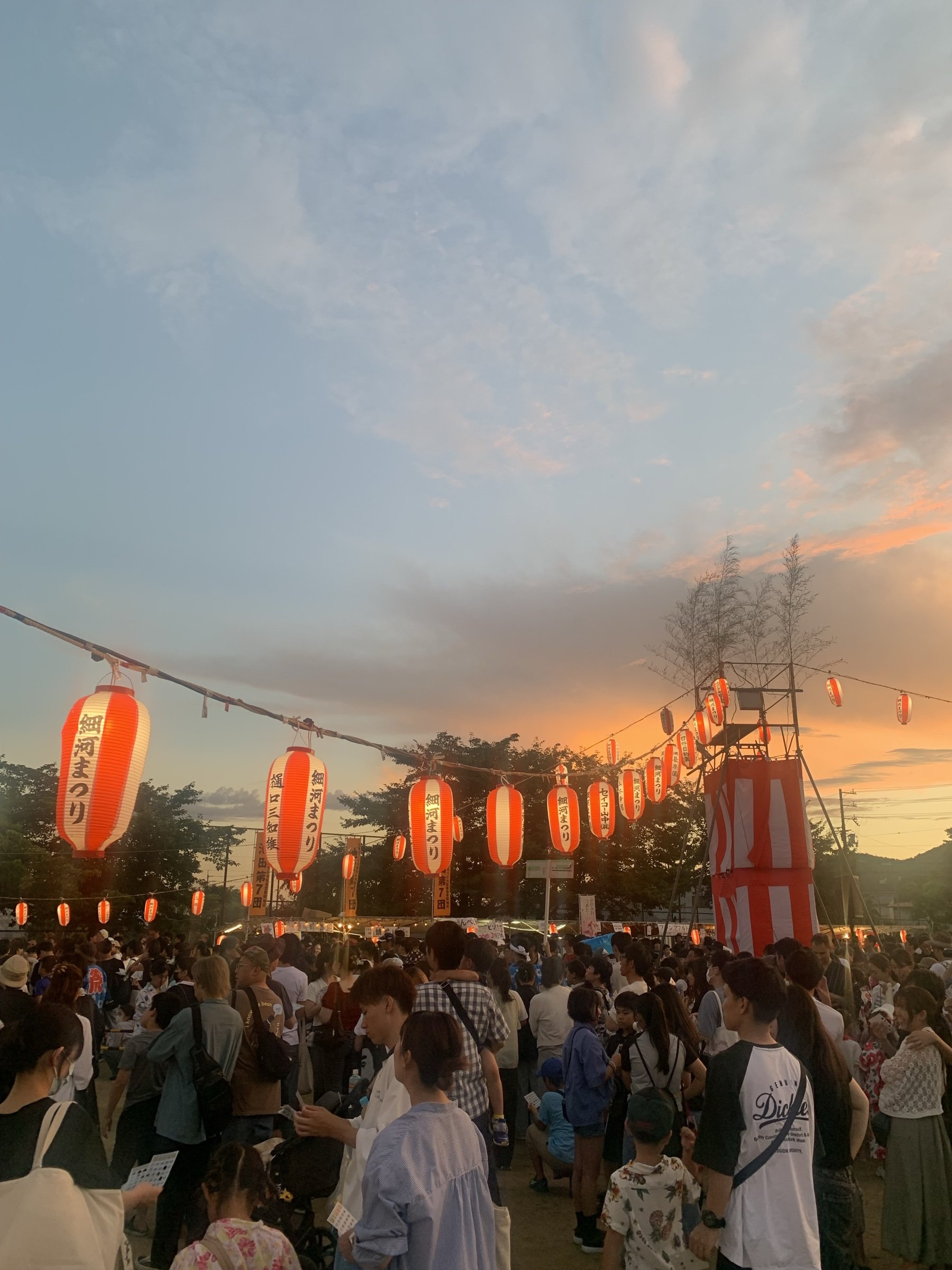 Red and white paper lanterns strung above a crowd at an evening summer festival.