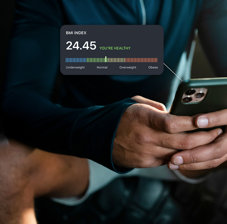 Person holding a smartphone displaying a workout app with exercise sets and reps, wearing a black digital watch, near gym equipment.