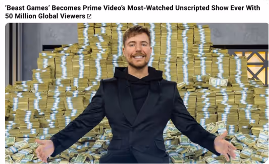 Man in a black suit sitting in front of large piles of stacked $100 bills with arms outstretched.