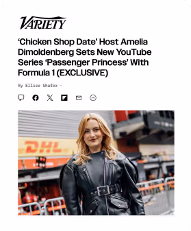 Amelia Dimoldenberg wearing a black leather jacket with a belt, standing at a Formula 1 event with DHL branding in the background.