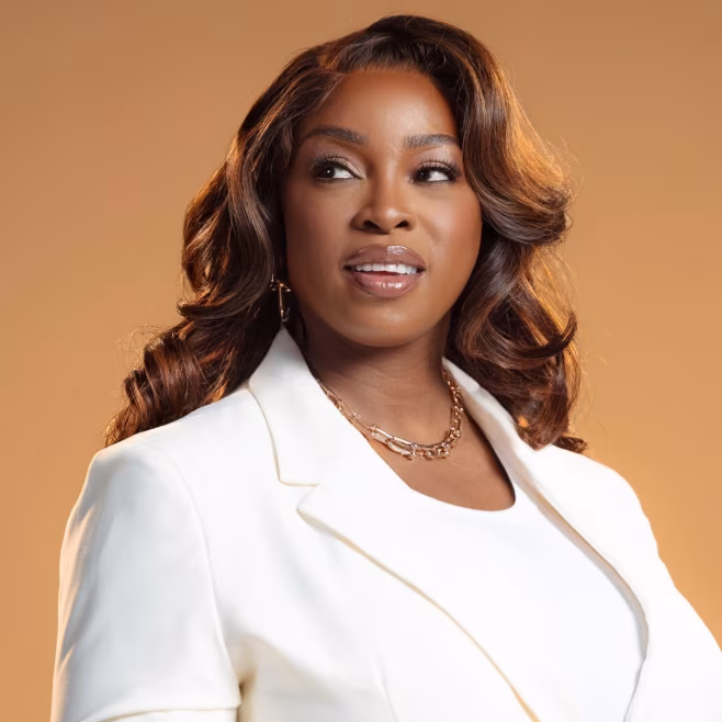 Confident woman with styled hair wearing white blazer and matching top against a beige background.