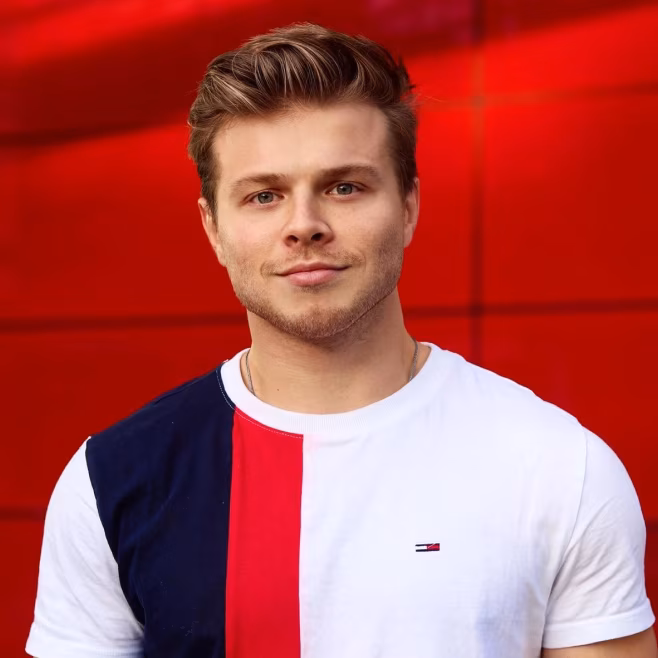 Young man with styled hair wearing a navy, red, and white color-blocked shirt against a red background.