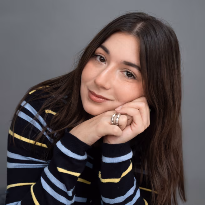Woman with long brown hair resting her chin on clasped hands, wearing a striped sweater.
