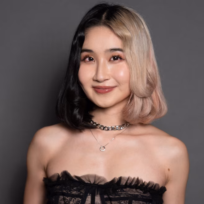 Smiling woman with half black, half blonde hair wearing a strapless black lace top and necklaces.