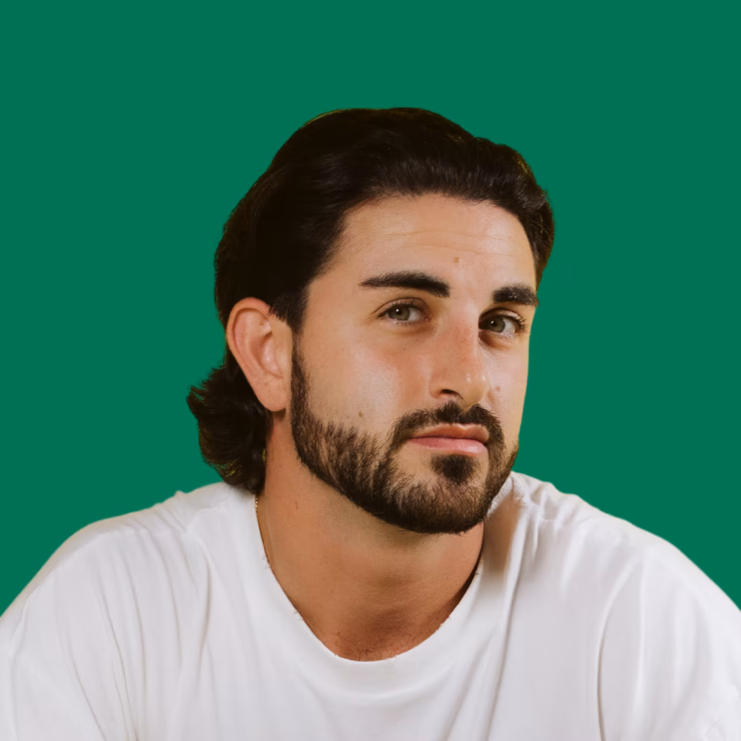 Portrait of a man with dark hair and beard wearing a white shirt against a solid green background.