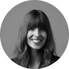 Black and white portrait of a woman with long hair and bangs smiling, framed in a circular crop.