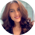 Smiling woman with long, wavy brown hair wearing hoop earrings and a necklace.