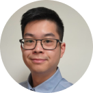 Portrait of a young man wearing glasses and a light blue shirt, smiling slightly and facing the camera.