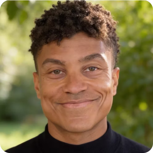Portrait of a smiling person with short curly hair and light brown eyes wearing a black high-neck shirt.