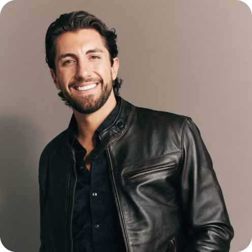 Smiling man with dark hair and beard wearing a black leather jacket over a black shirt.