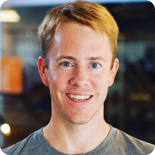 Smiling young man with short light brown hair and blue eyes wearing a gray shirt.