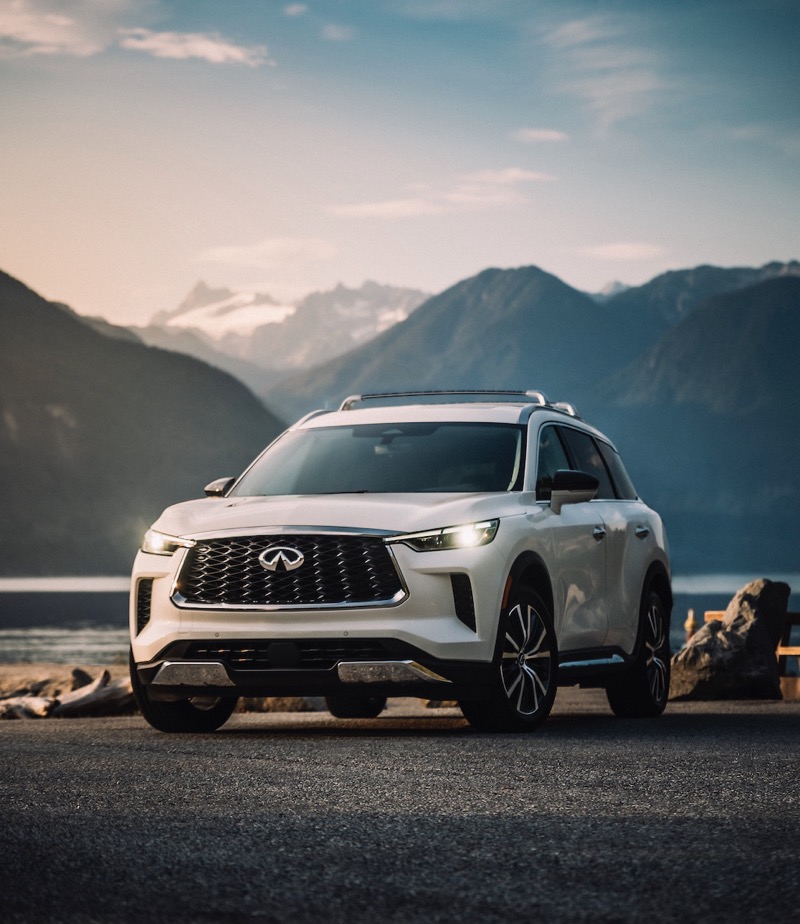 White Infiniti SUV parked on a paved surface with mountainous landscape and cloudy sky in the background during dusk.