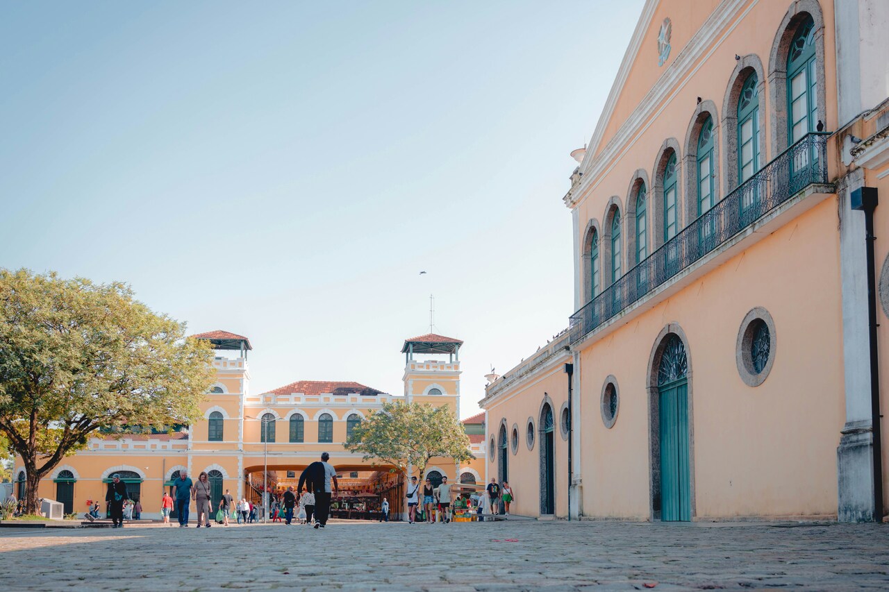 Historic yellow colonial buildings in a public square with people walking and shopping on a sunny day.