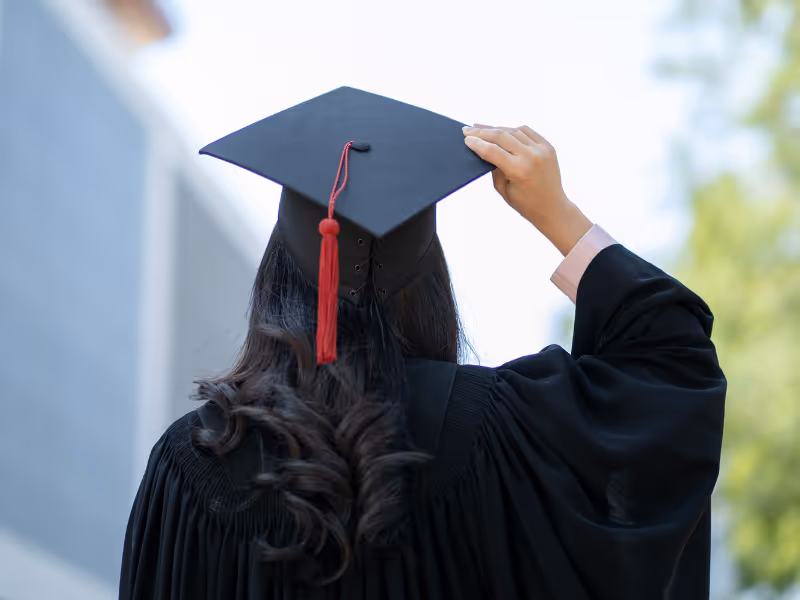 A female student holding her hat at graduation ceremony with her back to the camera