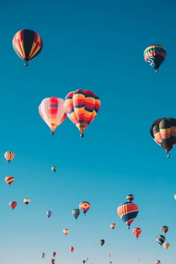 Numerous colorful hot air balloons floating in a clear blue sky.