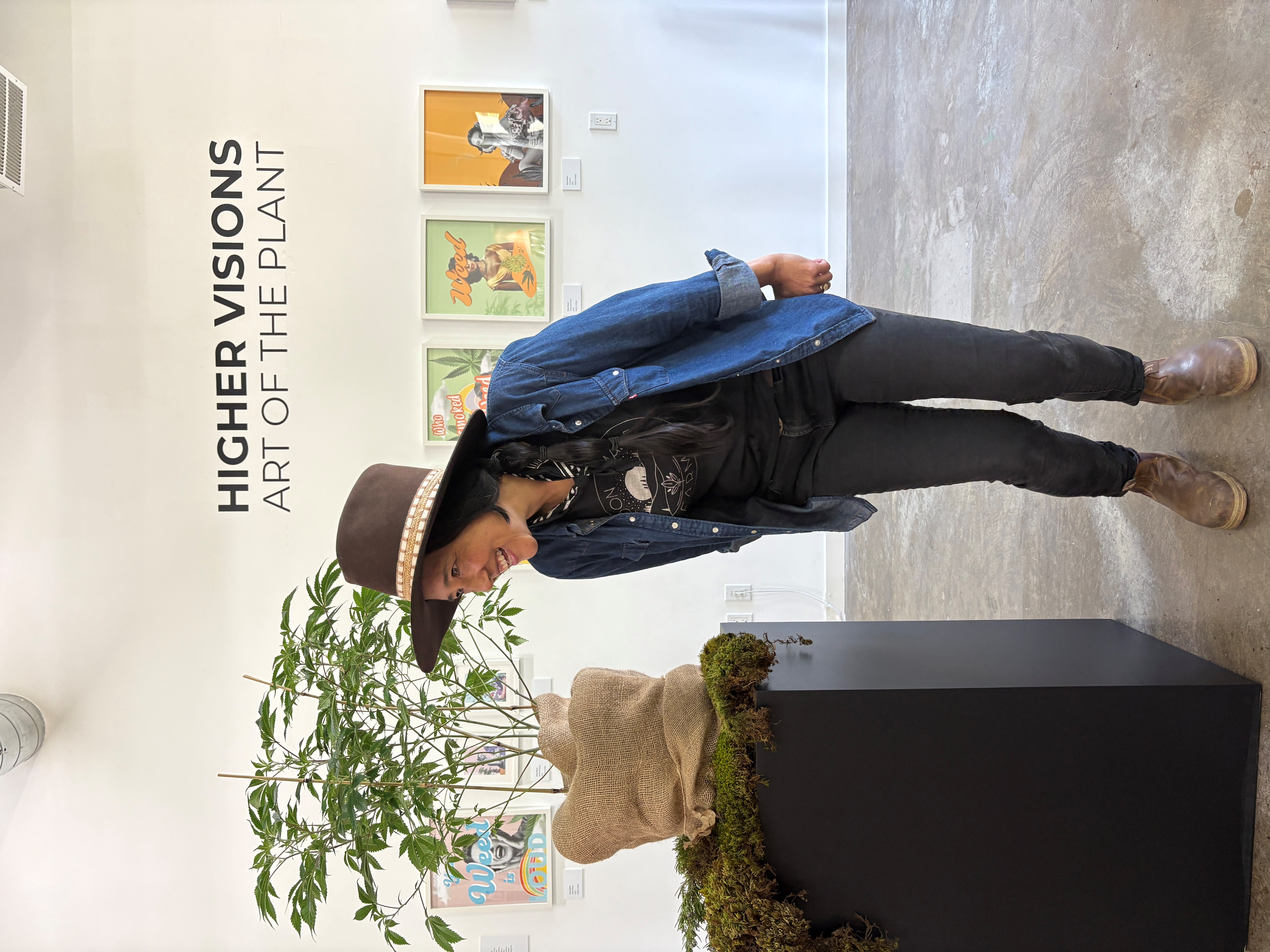 Tina Gordon of Moon Made Farms standing beside a cannabis plant exhibit at the Higher Visions Art of the Plant gallery.