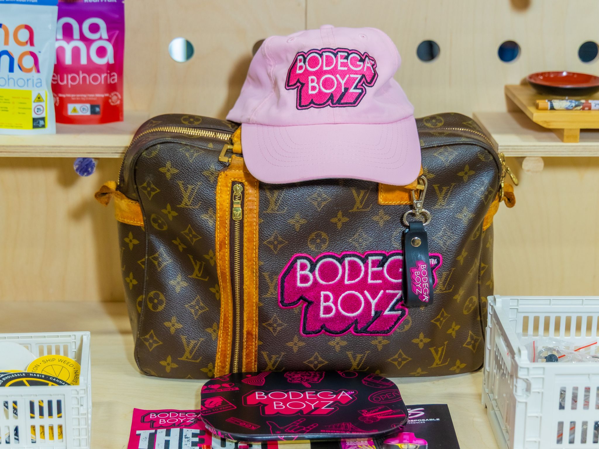 Pink Bodega Boyz cap resting on a vintage monogram duffel bag with a pink chenille Bodega Boyz patch and keychain.