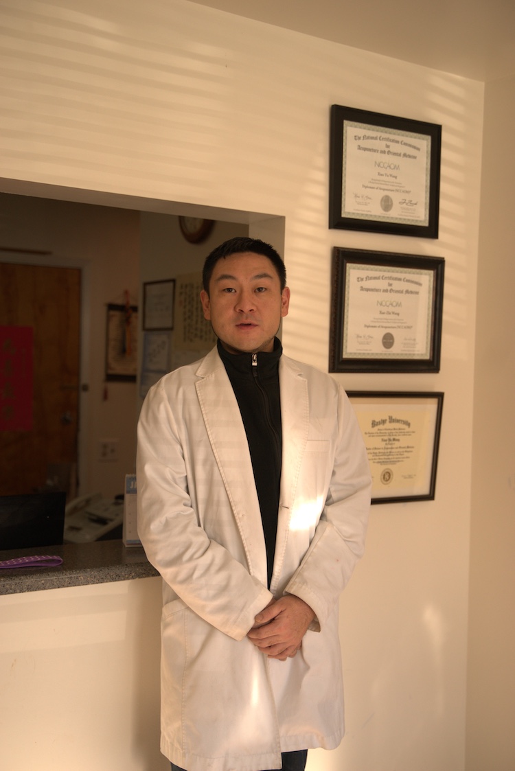Xiao Yu Wang, L.Ac., standing beside his NCCAOM and Bastyr University diplomas