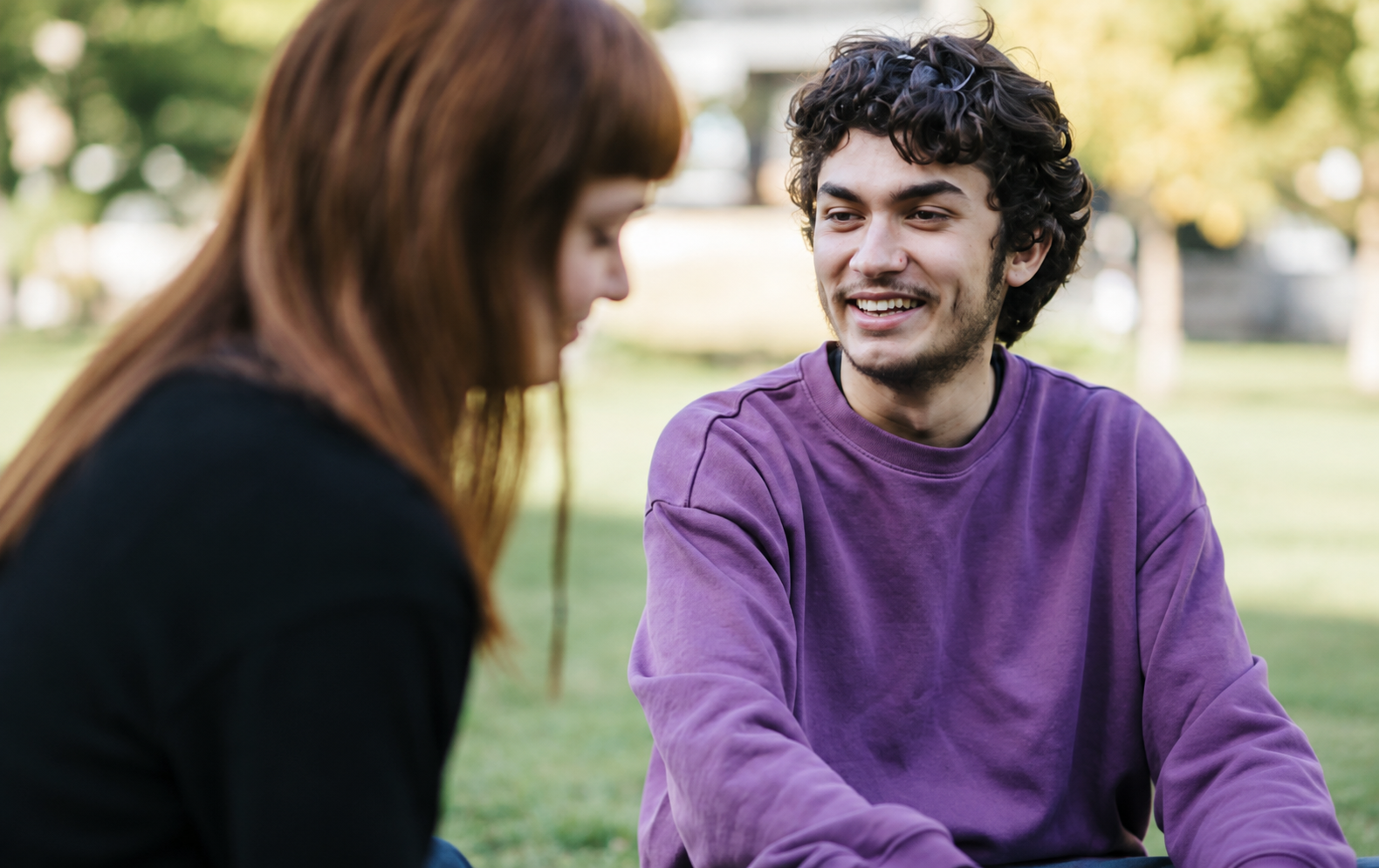 Two people smiling as they talk together outdoors.