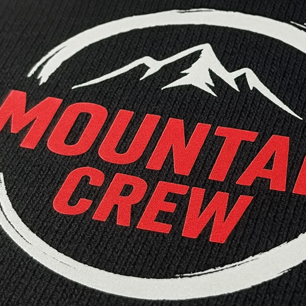Nahaufnahme eines Emblems mit Bergen und roter Schrift "Mountain Crew" auf schwarzem Textil
