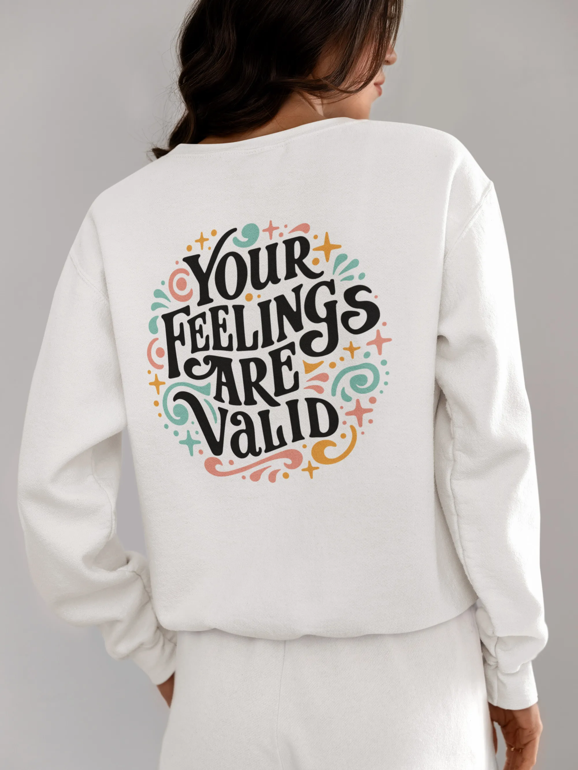 Woman wearing a white pullover hoodie with colorful text on the back that says 'Your feelings are valid.'