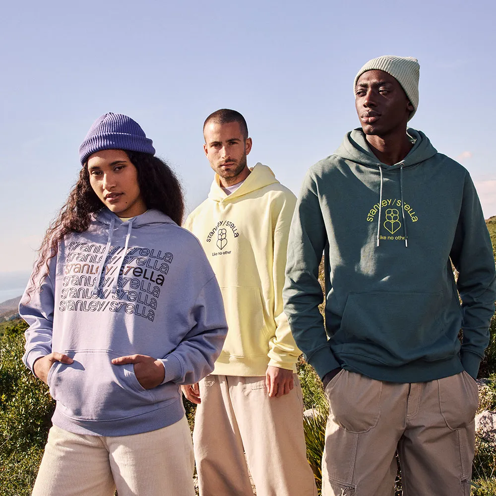 Three models outdoors wearing pastel-colored hoodies and beanies with 'Stanley/Stella' branding.