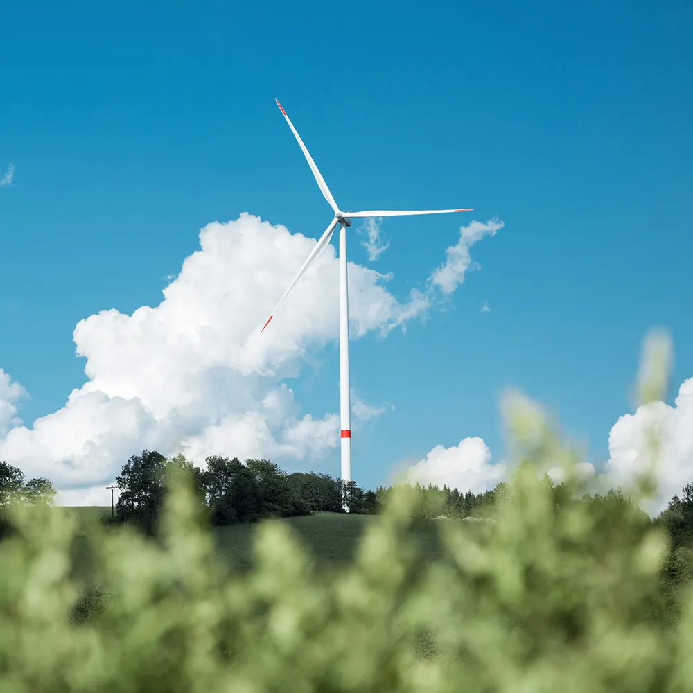 Single white wind turbine on a green hill under a blue sky with white clouds.