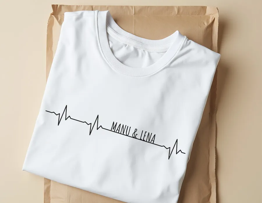 White T-shirt folded with a black heartbeat line graphic and the text 'MANU & LENA' integrated into the design.