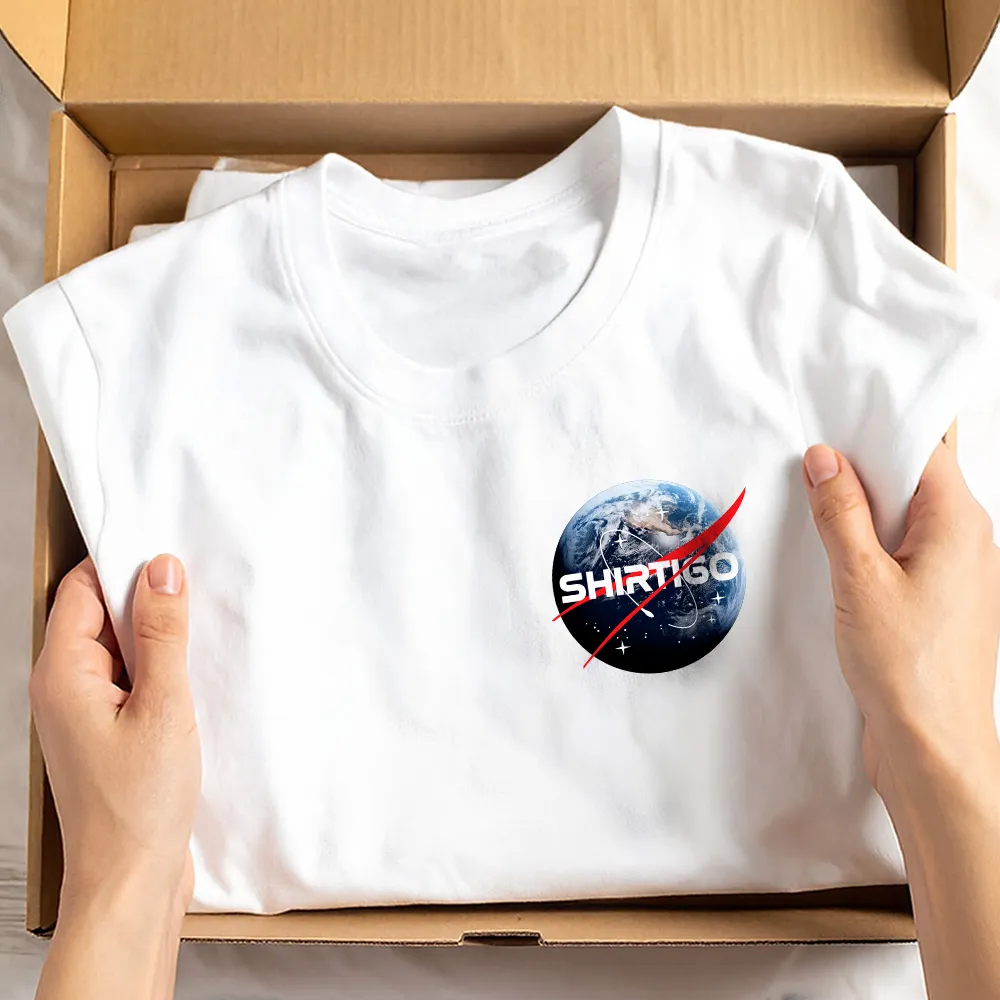 Hands holding white t-shirt with SHIRTIGO logo and earth graphic in cardboard box.