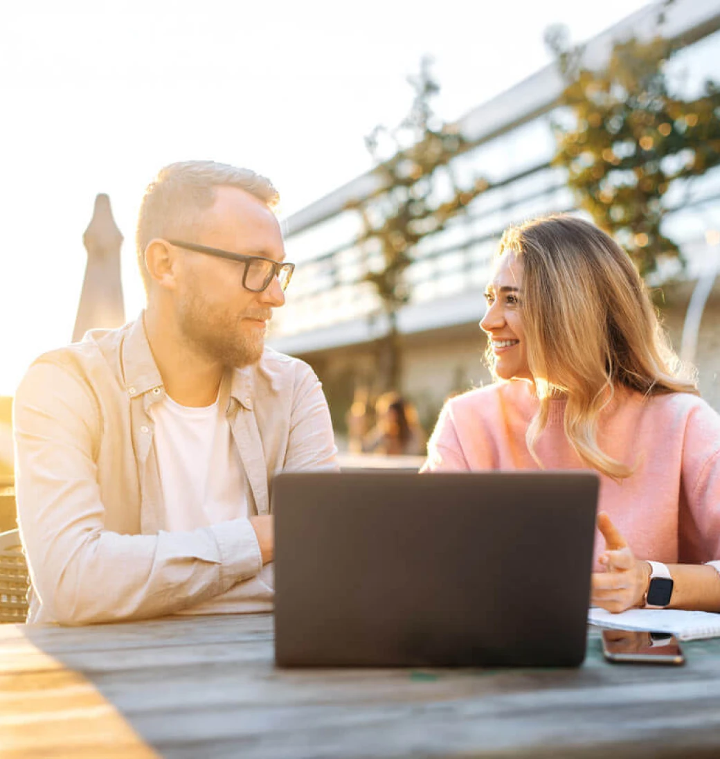 Et ungt par som sitter ute en fin sommerdag og ser på en laptop sammen.
