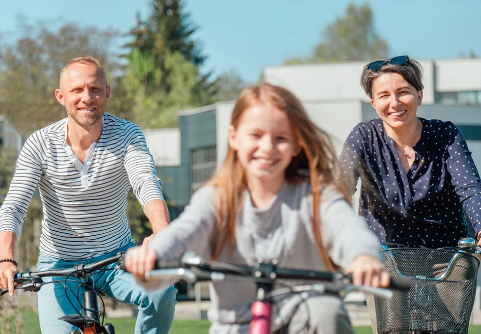En familie med to voksne og ett barn som er ute på sykkeltur sammen.